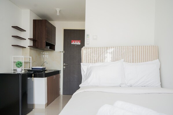 A hotel room with a bed, a small kitchenette, a door, and a wall-mounted control panel. - Comfy And Minimalist Studio Room At Serpong Garden Apartment (Cisauk)