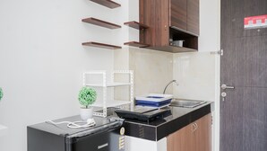 A compact kitchen with a black refrigerator, a sink, and wooden cabinets. - Comfy And Minimalist Studio Room At Serpong Garden Apartment (Cisauk)