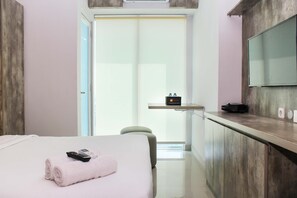 Quarto de hotel com uma cama, uma escrivaninha, uma cadeira, uma televisão e um banheiro visível por uma porta aberta.
