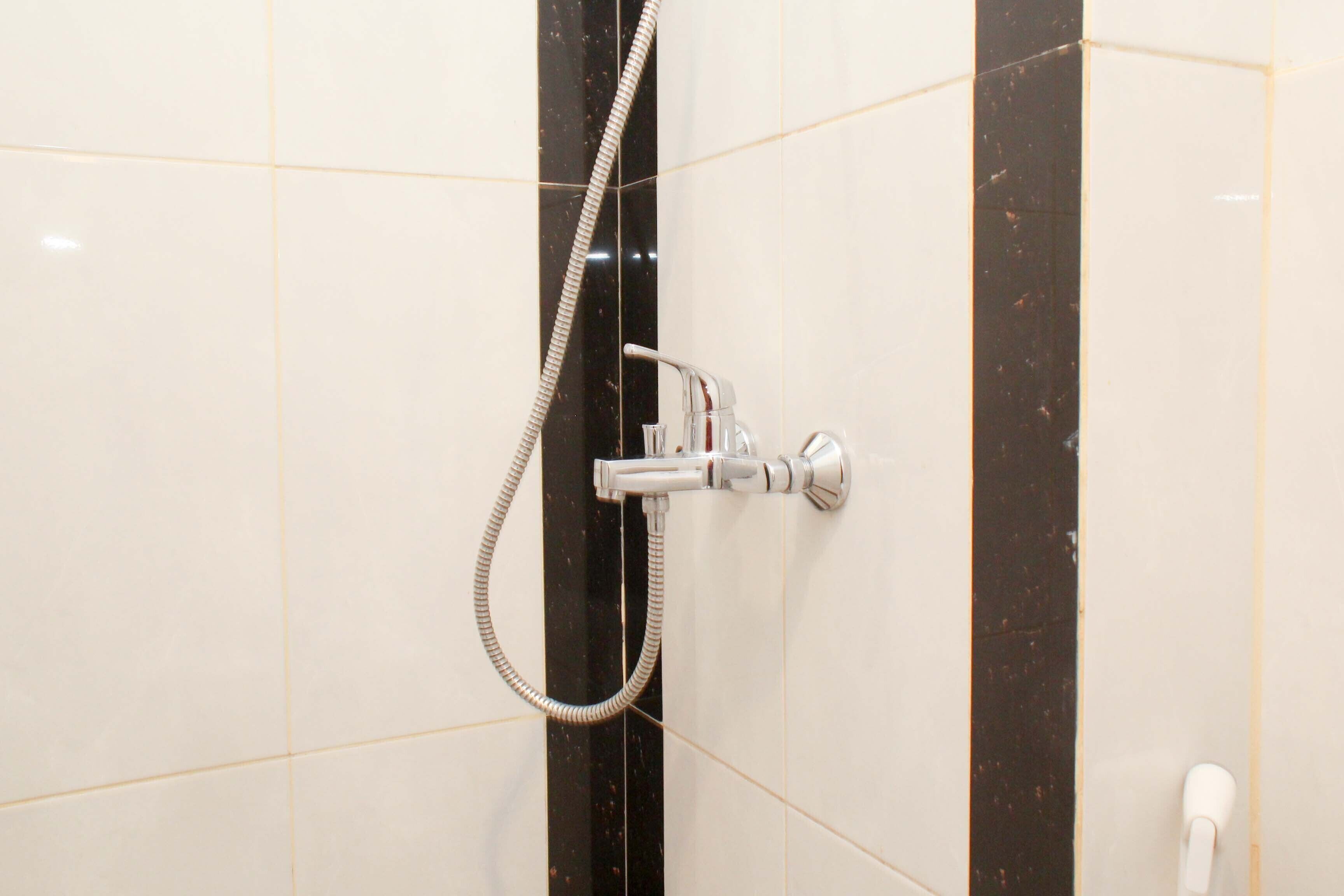 Une douche équipée d’un pommeau de douche à main et d’un flexible, le tout fixé sur un mur recouvert de carreaux blancs et noirs.