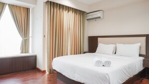 A hotel room with a large bed, a window with curtains, an air conditioning unit, and a wooden floor. - Minimalist And Comfort Studio At Tamansari The Hive Apartment (Jakarta)