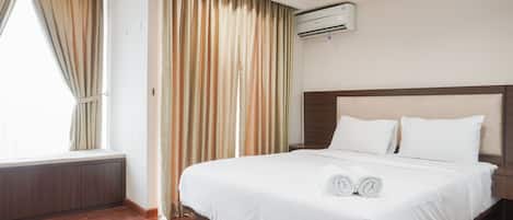 Ein Hotelzimmer mit einem großen Bett, einem Fenster mit Vorhängen, einer Klimaanlage und einem Holzboden.