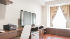 A hotel room with a wooden desk, a television, a minibar, and a window with curtains. - Minimalist And Comfort Studio At Tamansari The Hive Apartment (Jakarta)