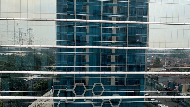 A modern glass building with a grid-like facade and a hexagonal pattern at the base. - Minimalist And Comfort Studio At Tamansari The Hive Apartment (Jakarta)