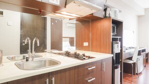A modern kitchen with a stainless steel sink, double faucets, a built-in stove, and wooden cabinets. - Minimalist And Comfort Studio At Tamansari The Hive Apartment (Jakarta)