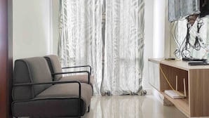 Ein modernes Zimmer mit grauem Sofa, einem an der Wand befestigten Fernseher und einem Schreibtisch mit Computer und Kabeln.