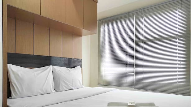 Ein Hotelzimmer mit Bett, weißer Bettwäsche, einem Kopfteil und einem Fenster mit Jalousien.