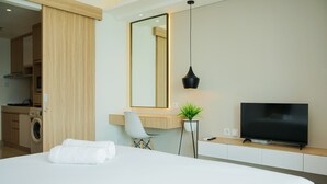A hotel room with a bed, a desk with a chair, a TV, a mirror, and a washing machine in the background.