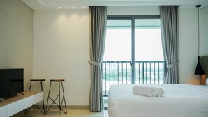 A hotel room with a bed, a TV, two stools, and a large window with curtains.