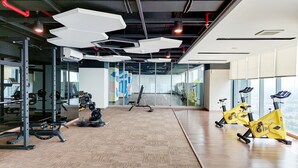 Ein Fitnessstudio mit Trainingsgeräten, einem Spiegel und Blick auf die Stadt.