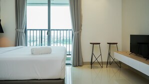Ein Hotelzimmer mit Bett, zwei Hocker, einem Fernseher und einem Balkon mit Vorhängen.