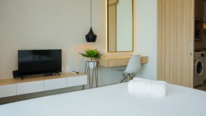 Ein modernes Hotelzimmer mit Flachbildfernseher, Topfpflanze, Schreibtisch, Stuhl, großem Spiegel und Waschmaschine.