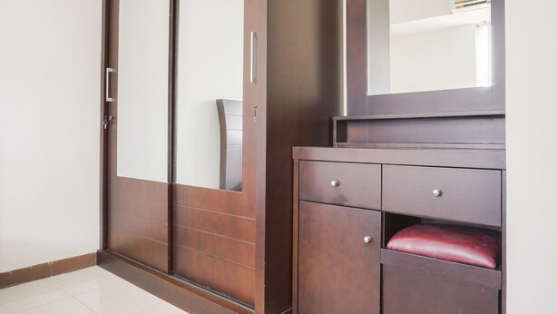 A wooden wardrobe with a mirror, a red cushioned seat, and a tiled floor. - Cozy Stay 1Br At Maple Park Apartment Near Sunter (Jakarta)