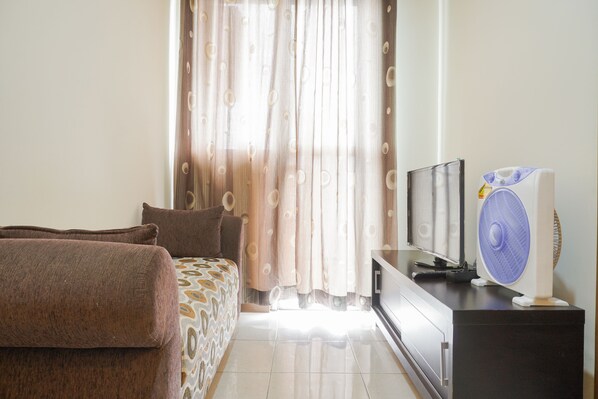 A bedroom with a bed, a TV, a fan, and curtains.
