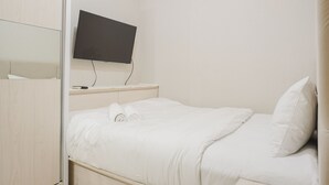 A hotel room with a bed, a TV mounted on the wall, and a wooden wardrobe. - Comfort And Simply 2Br At Green Bay Pluit Apartment (Jakarta)