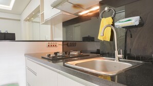 A kitchen with a stainless steel sink, a yellow towel hanging on the faucet, and a dish rack on the wall. - Comfort And Simply 2Br At Green Bay Pluit Apartment (Jakarta)