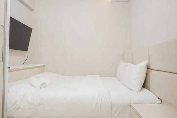 Ein weißes Bett mit Kopfteil, ein Nachttisch und ein an der Wand befestigtes Flachbildfernsehen.