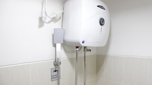 Um aquecedor de água fixado na parede, com painel de controle, torneira e placa de aviso.