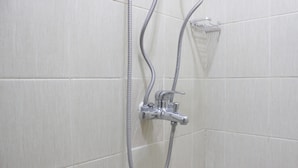 Chuveiro com um chuveiro de mão e um chuveiro fixo, ambos instalados numa parede revestida de azulejos.