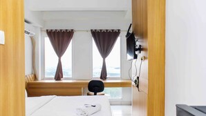 Ein Hotelzimmer mit Bett, Schreibtisch, Stuhl, Fernseher und einem Fenster mit Vorhängen.