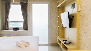 Ein Hotelzimmer mit Bett, Fernseher an einer Holzwand, einer Tür und einem Fenster mit Vorhängen.