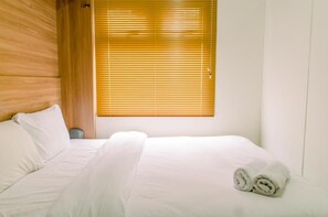 Habitación de hotel con cama, ropa de cama blanca y ventana con persianas horizontales.