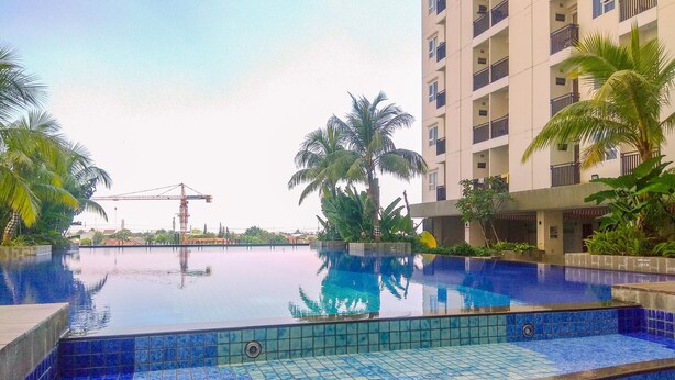 A swimming pool with blue tiles, surrounded by palm trees and a multi-story building.