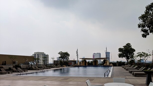 A rooftop pool area with lounge chairs and tables, surrounded by buildings and trees.