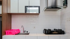 A kitchen with white cabinets, a stainless steel range hood, a sink, and a pink basket. - Minimalist And Warm Studio Casa De Parco Apartment (Pagedangan)