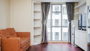 A modern living room with a brown leather sofa, a large window with curtains, a flat-screen TV, and built-in shelving.