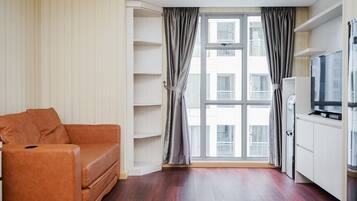 A modern living room with a brown leather sofa, a large window with curtains, a flat-screen TV, and built-in shelving.