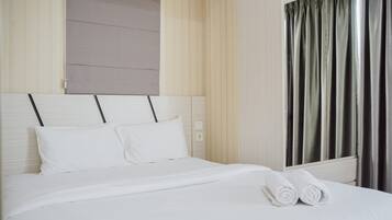 A neatly made bed with white linens and pillows, a headboard with a light wood finish, and a window with dark curtains.