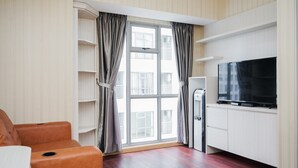 A modern living room with a flat-screen TV, a sofa, and a large window with curtains.