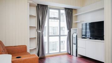 A modern living room with a flat-screen TV, a sofa, and a large window with curtains.