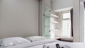 Ett hotellrum med en säng, en fjärrkontroll och ett fönster med utsikt över byggnader.
