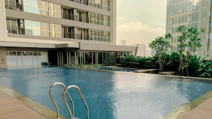 A modern building with a swimming pool, surrounded by greenery and a wooden deck.