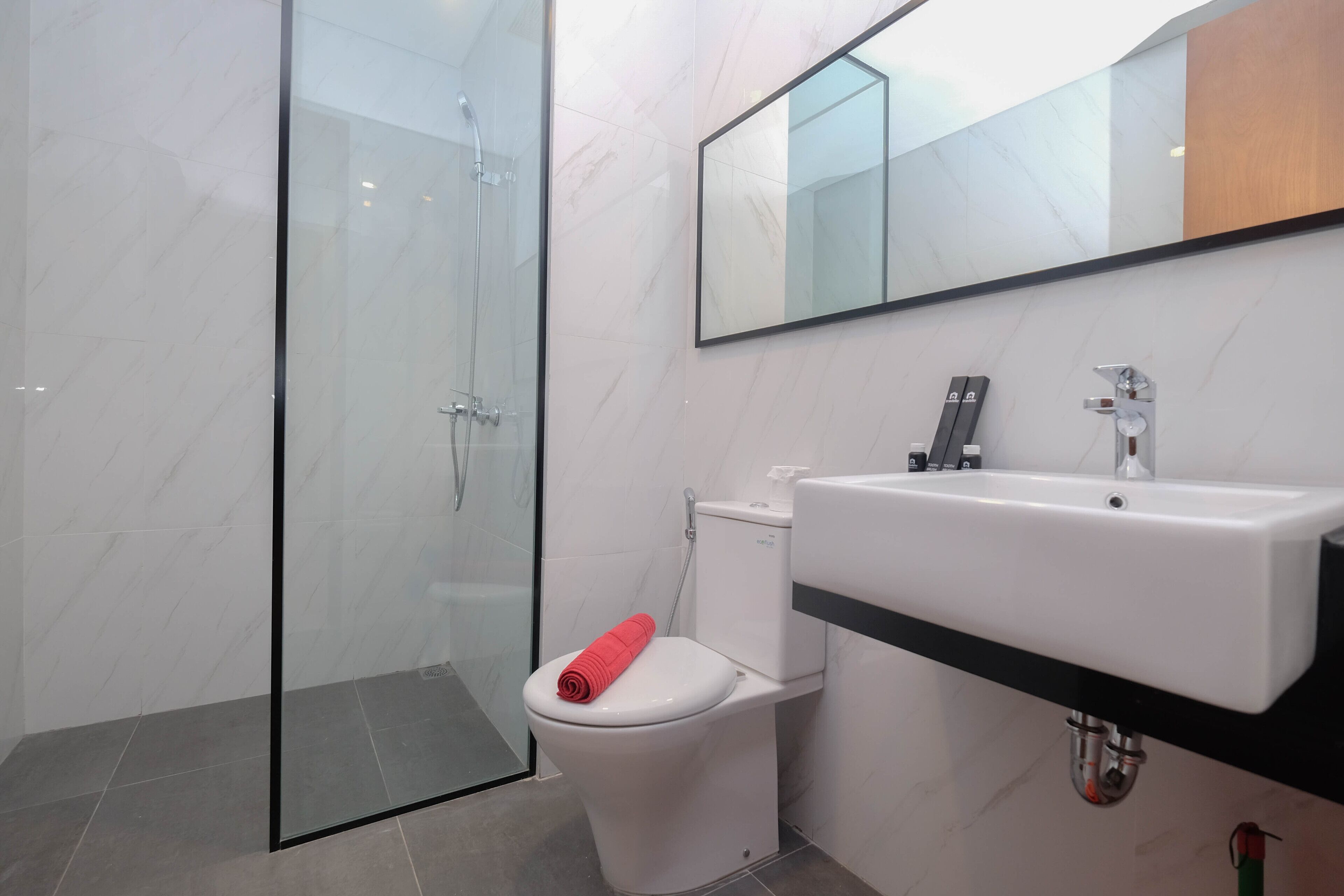 A modern bathroom with a glass shower enclosure, a white toilet with a red towel, and a large sink with a mirror above it.