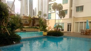 A swimming pool surrounded by greenery and modern buildings. - Minimalist And Comfort Studio Apartment At Springhill Terrace Residence (Jakarta)