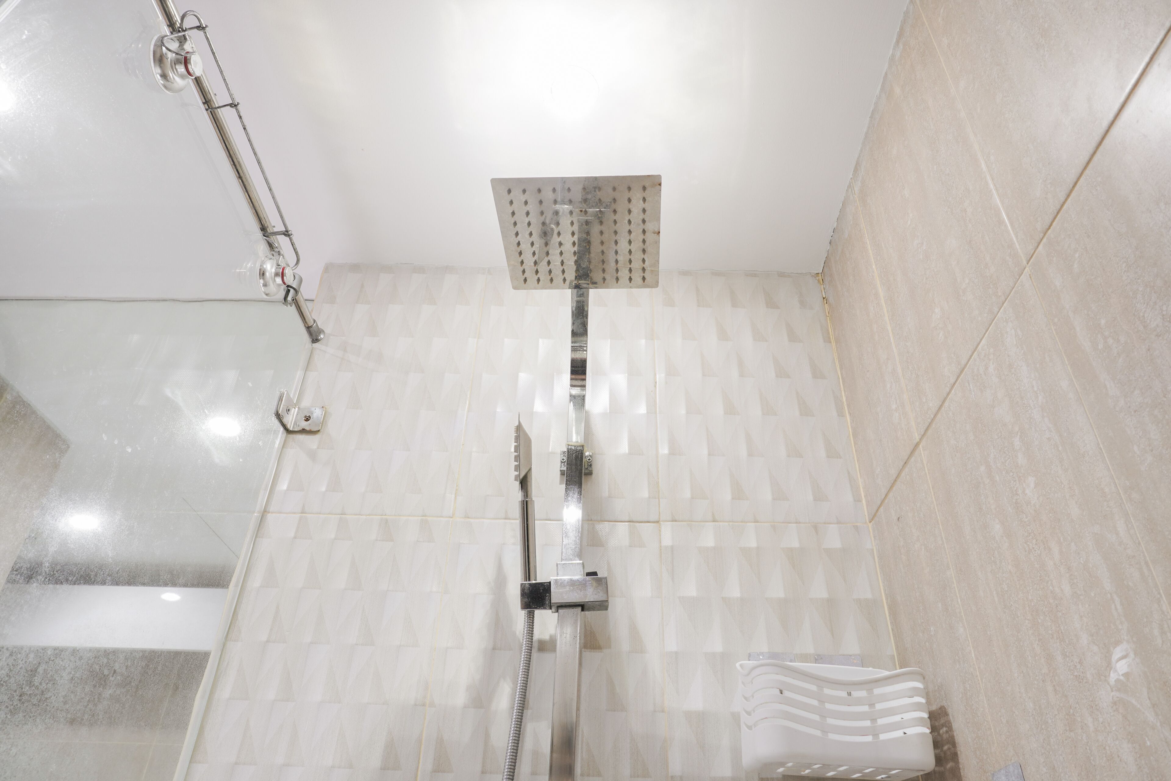 Ducha con cabezal de ducha manual y otro fijo, paredes con azulejos y un perchero para toallas.