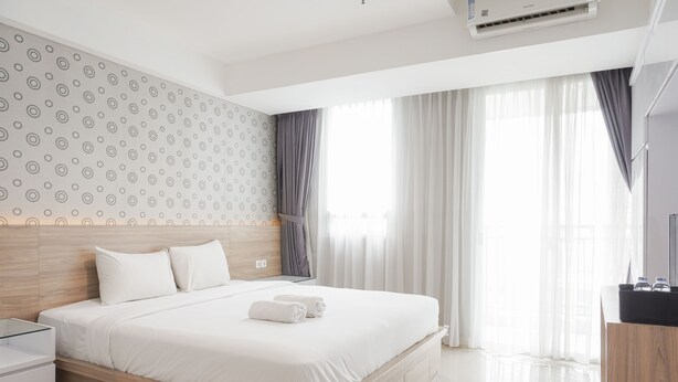 A modern hotel room with a wooden headboard, a neatly made bed, a bedside table, and a large window with curtains. - Minimalist And Comfort Studio Apartment At Springhill Terrace Residence (Jakarta)