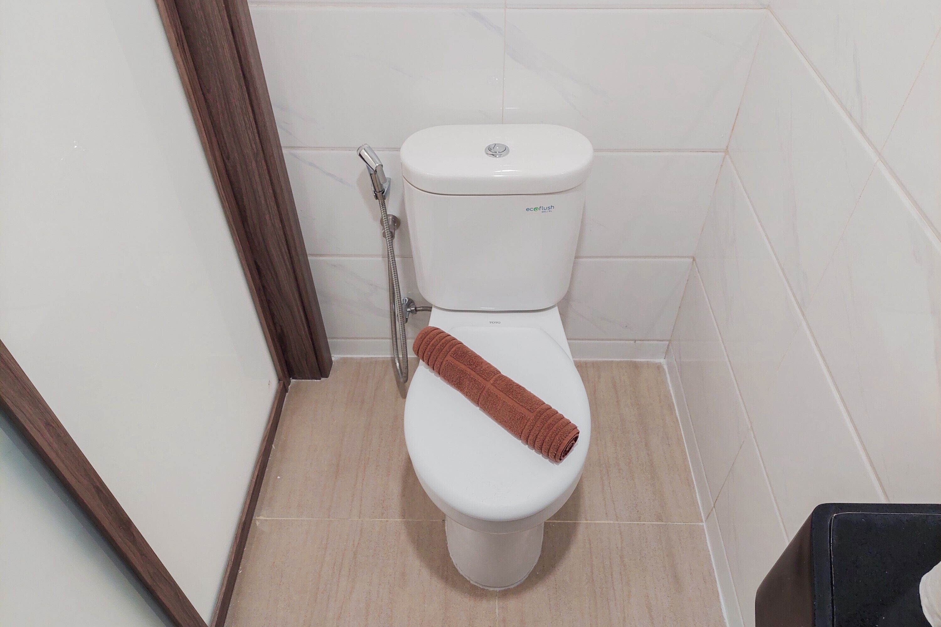 Des toilettes blanches avec une serviette marron posée sur la cuvette, une pomme de douche et un mur carrelé.