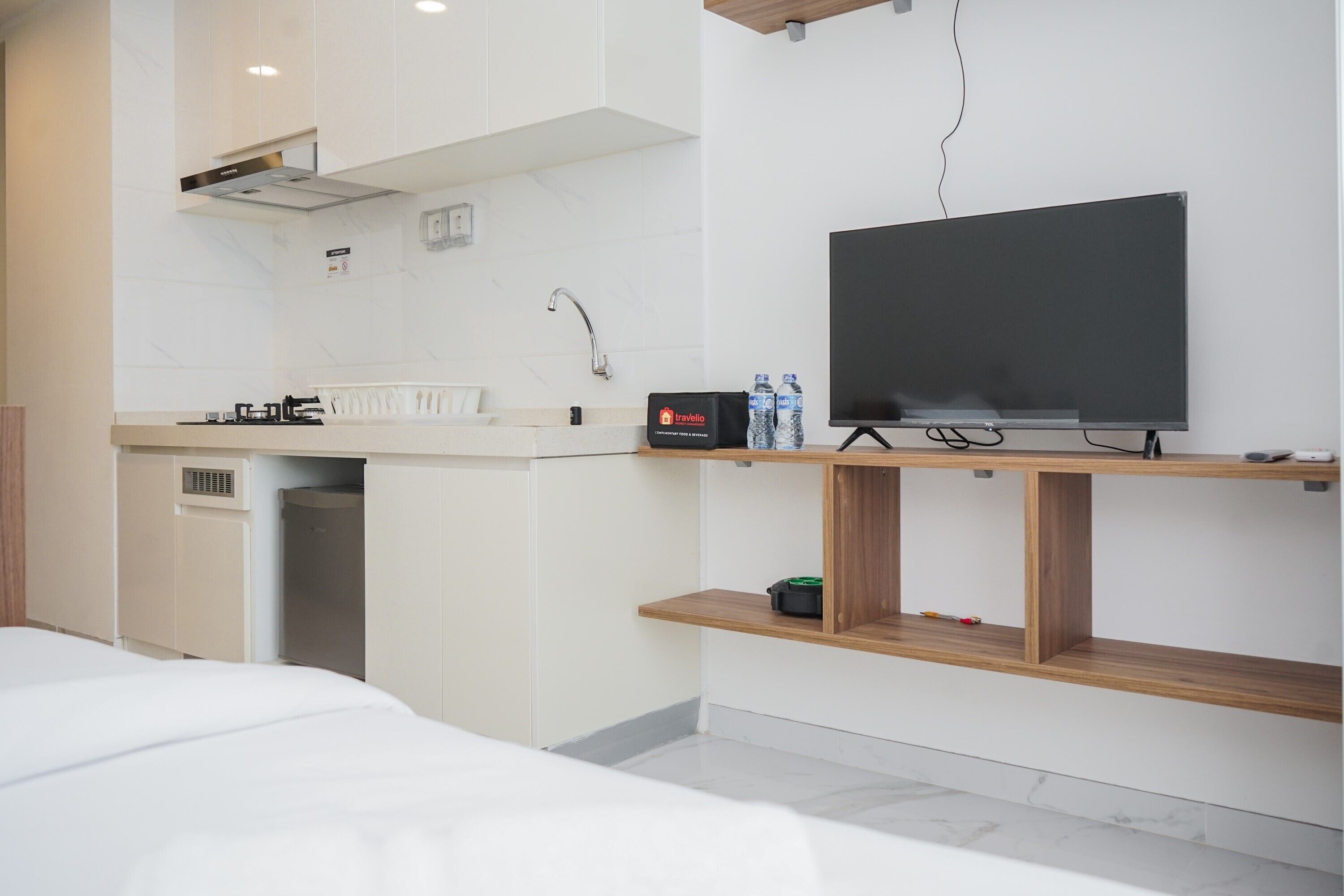 A modern hotel room with a kitchenette, a flat-screen TV, and a bed.