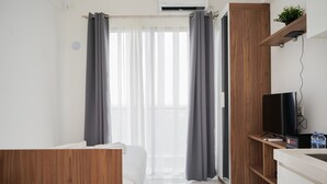 A modern hotel room with a bed, a TV, a wooden cabinet, and a window with curtains. - Nice And Comfort Studio Room At Sky House Bsd Apartment (Pagedangan)
