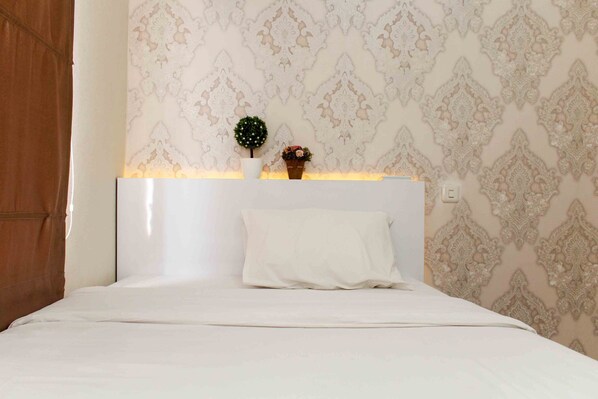 Un lit bien fait, avec une tête de lit blanche, une petite plante en pot et un objet décoratif posé sur la tête de lit.