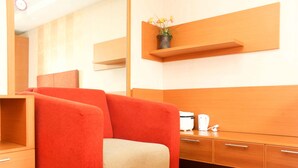 A modern hotel room with a red sofa, wooden furniture, and a small plant on a shelf. - Cozy Stay Studio Apartment (No Kitchen) At Metropark Condominium Jababeka (Cikarang)