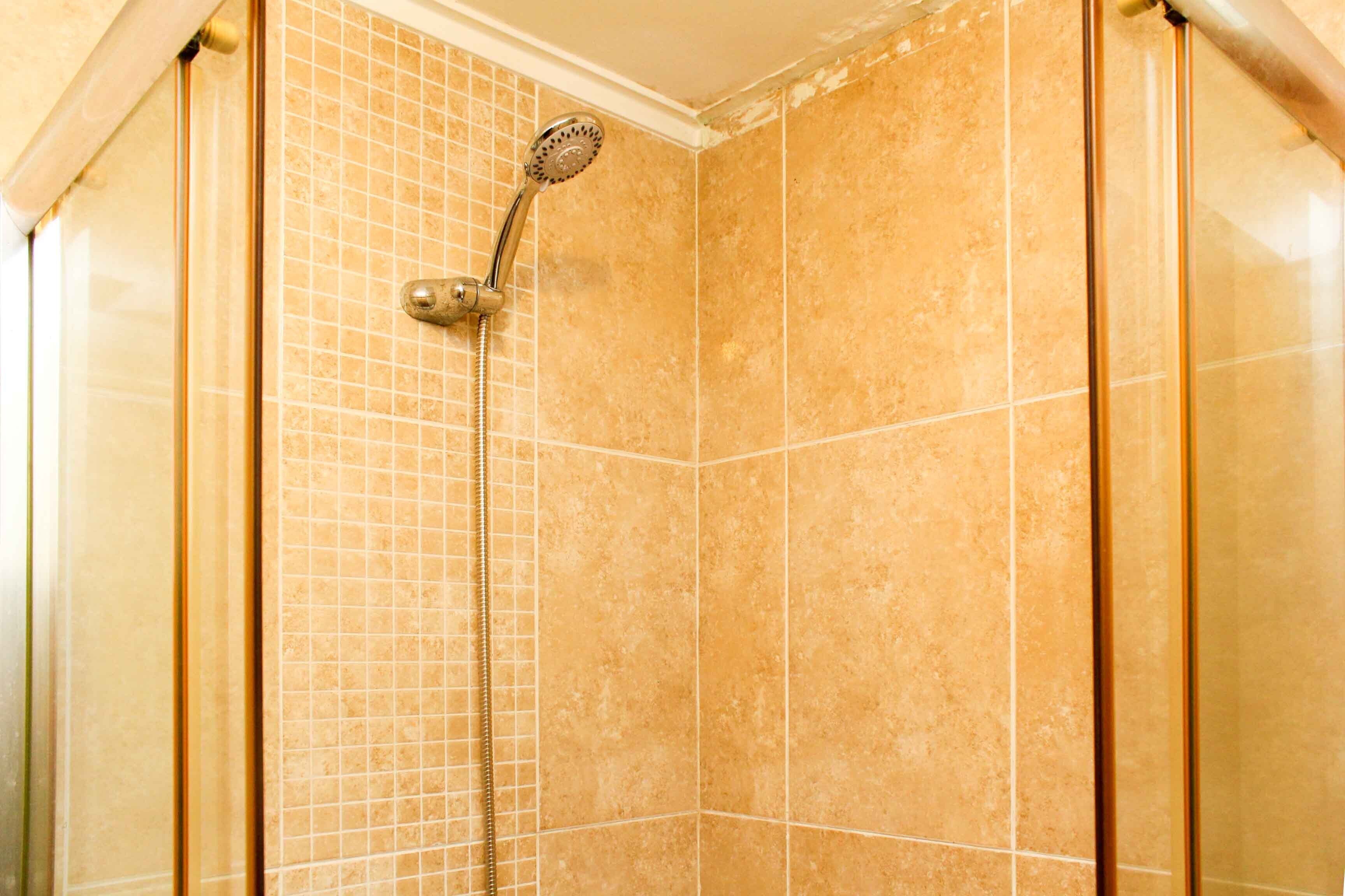 Ducha con azulejos color beige y un cabezal de ducha de mano.