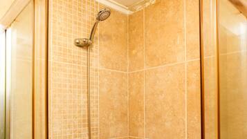 Ducha con azulejos color beige y un cabezal de ducha de mano.