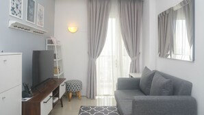 A modern living room with a grey sofa, a wooden coffee table, a TV, and a bookshelf. - Modern And Comfort 2Br Apartment At Signature Park Grande (Jakarta)