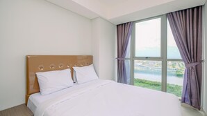 A bedroom with a large bed, a nightstand, and a window with curtains. - Comfortable And Minimalist 2Br At Gold Coast Apartment (Jakarta)