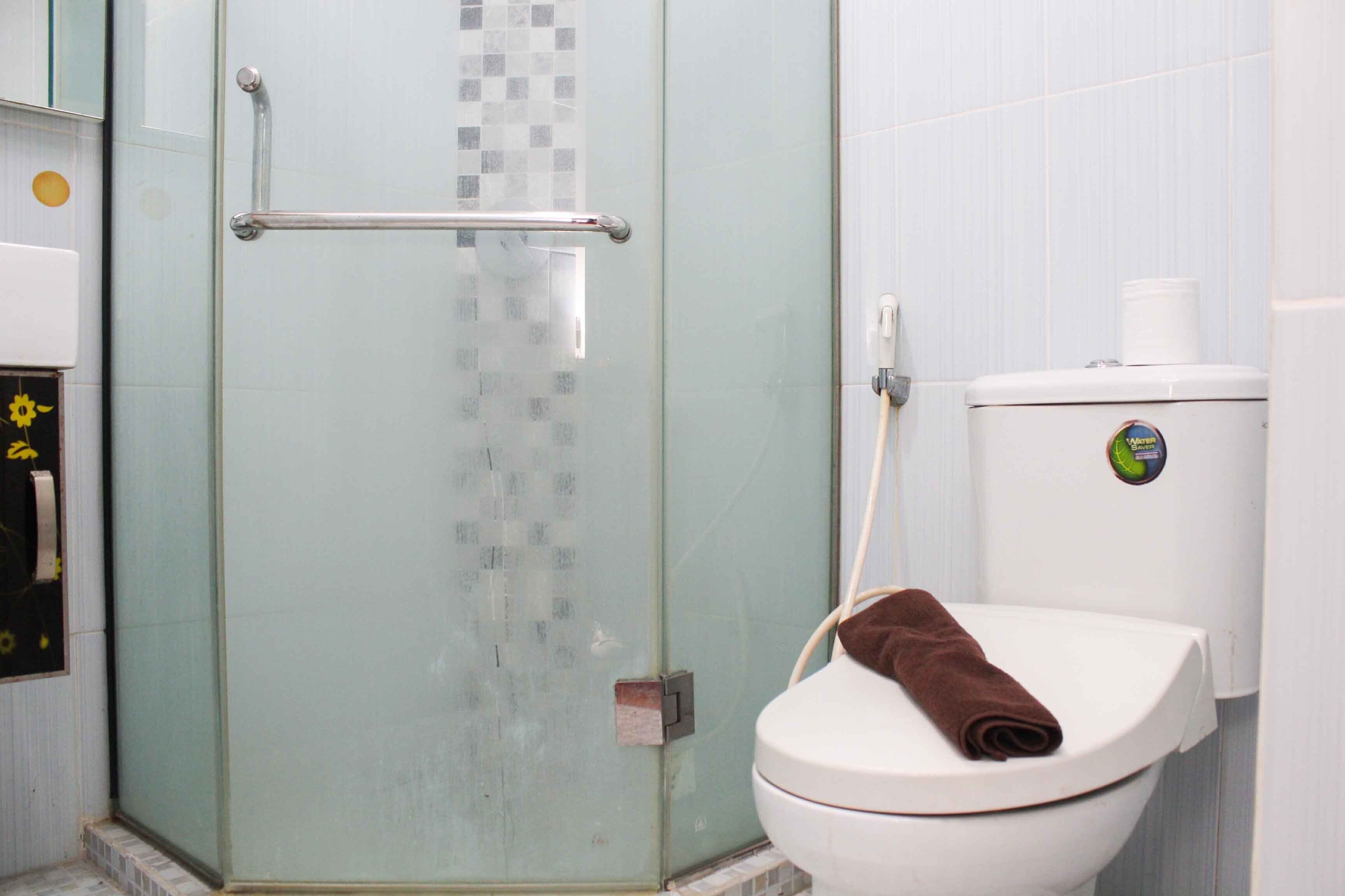 A bathroom with a glass shower enclosure, a white toilet, and a towel on the seat.